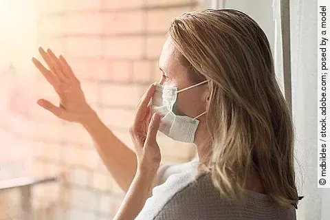 Social-Dinstancing, Frau mit Maske am Fenster