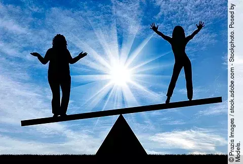 2 Frauen stehen auf einer Wippe, rechts ohne, links mit Übergewicht