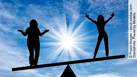 2 Frauen stehen auf einer Wippe, rechts ohne, links mit Übergewicht