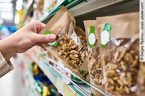 Frau greift nach verpackten Walnüssen im Supermarkt.