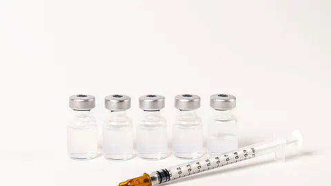 5 Ampullen mit Impfserum und 1 Spritze vor weißem Hintergrund