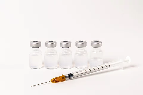 5 Ampullen mit Impfserum und 1 Spritze vor weißem Hintergrund