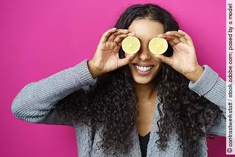 Lachende Frau hält sich Zitronenscheiben vor die Augen