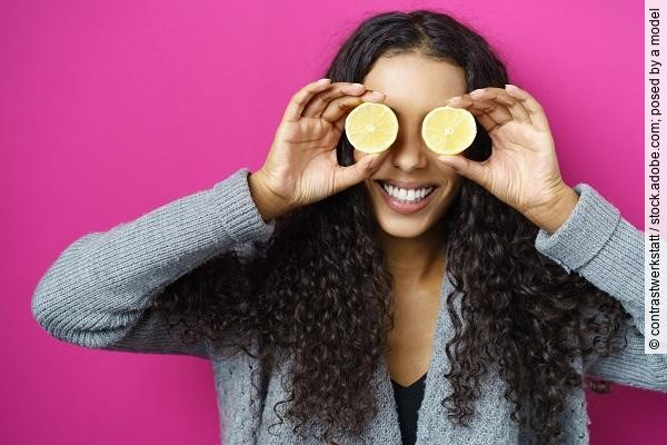 Lachende Frau hält sich Zitronenscheiben vor die Augen