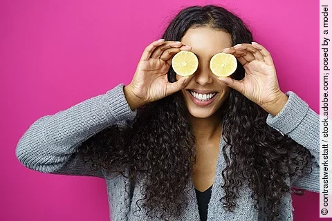 Lachende Frau hält sich Zitronenscheiben vor die Augen