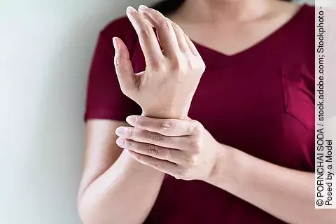 Frau mit dunkelrotem T-Shirt hält sich das Handgelenk