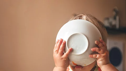 blond kid boy, very hungry eats and holds a plate with both hand Kleinkind leckt seinen Teller ab