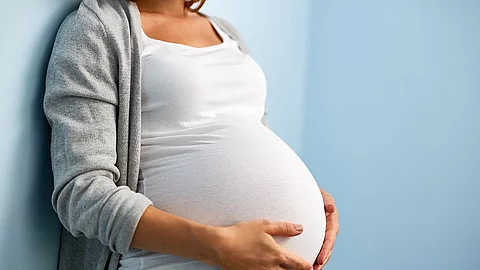 Mid-section portrait of unrecognizable woman during last months of pregnancy holding her big belly gently standing against wall in blue room Schwangerschaft, Frau, Babybauch