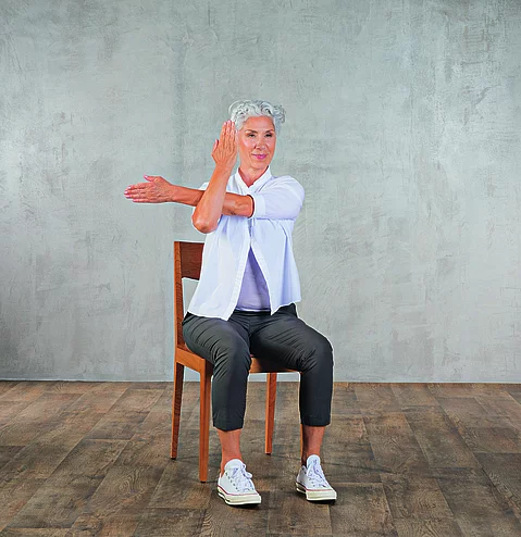 Frau im mittleren Alter praktiziert Yoga auf einem Stuhl aus Holz.