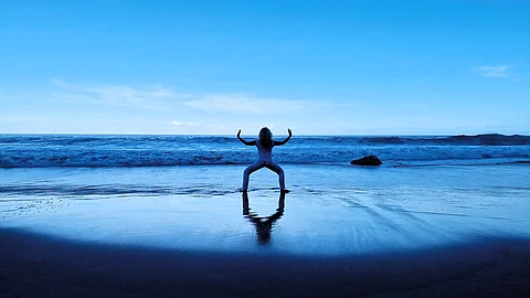 Frau (von hinten zu sehen) macht Qigong am Meer
