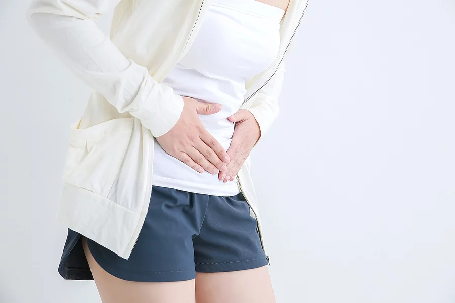 Junge Frau in Sportkleidung hält sich den Unterbauch