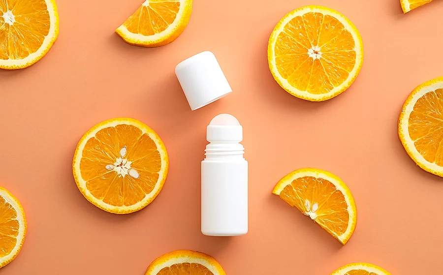 Weißer Deo-Roller sowie zahlreiche ganze und halbe Orangenscheiben vor orangenem Hintergrund.