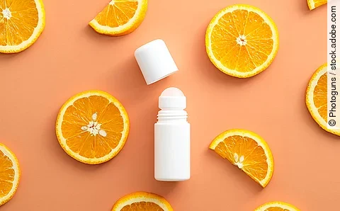 Weißer Deo-Roller sowie zahlreiche ganze und halbe Orangenscheiben vor orangenem Hintergrund.