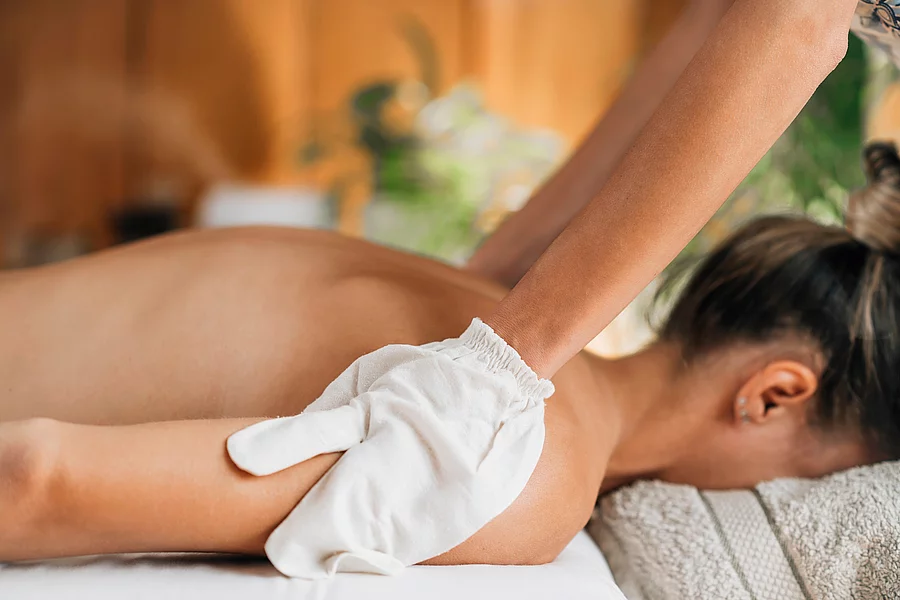 Ayurveda Garshana Massage, Dry Massaging Technique with Raw Silk Frau liegt auf dem Bauch auf Massageliege, ayurvedische Ölmassage