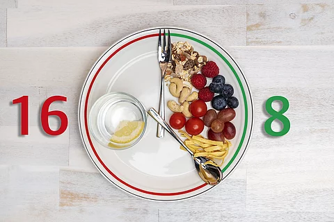 Besteck als Zeiger einer Uhr auf einem Teller: zwischen 12 und 4 Uhr liegen Lebensmittel