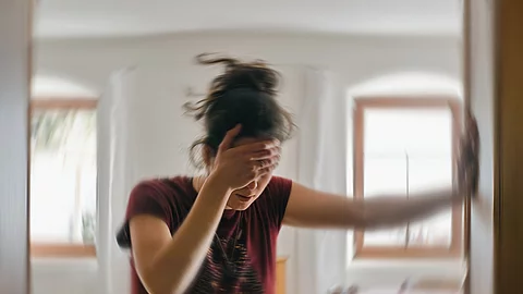 Frau steht im Türrahmen und hält die Hände vor die Augen, Migräneattacke