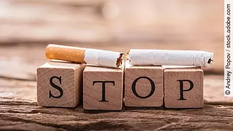 Holzbausteine bilden das Wort Stop. Auf ihnen liegt eine auseinander gebrochene Zigarette.