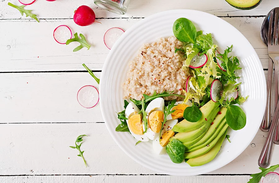 Healthy breakfast. Dietary menu. Oatmeal porridge and avocado sa Haferporridge mit Avocado, Ei und Radieschen auf einem Teller angerichtet
