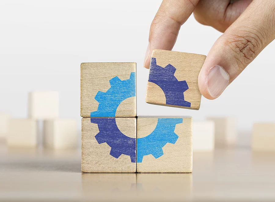 Hand putting the last piece of wooden blocks with the gear icon. Team work, unity, partnership or integration concept. Ein letztes Puzzlestück in Form von einem Holzklotz wird zusammengefügt.