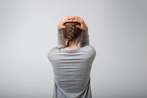 Stehende Frau von hinten, hält sich den Kopf
