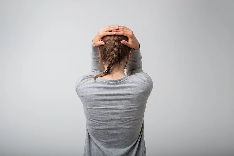 standing young woman, back view. She is holding her head in depression. Concept of negative despair emotion Stehende Frau von hinten, hält sich den Kopf