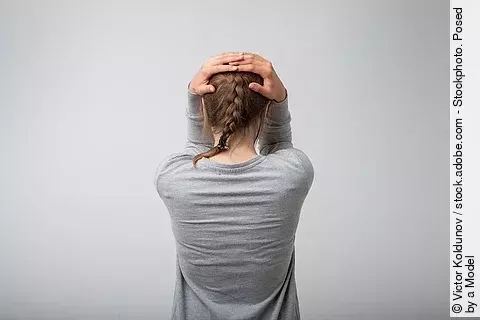 Frau in Rückenansicht, hält sich die Hände über dem Kopf