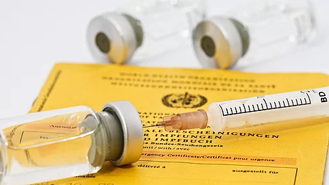 Auf einem Impfpass liegen mehrere Impffläschchen und eine Injektionskanüle.