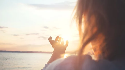Frau streckt ihre Hand Richtung Sonne aus. 