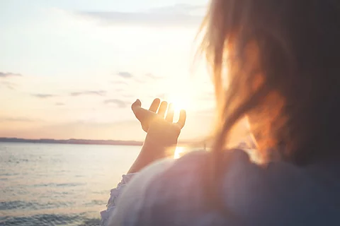Frau streckt ihre Hand Richtung Sonne aus. 