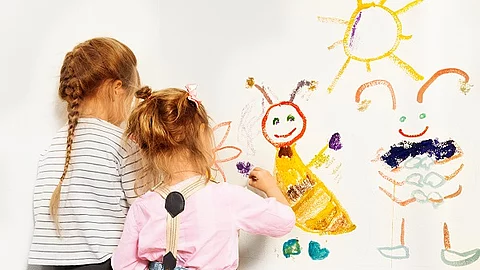 Zwei kleine Mädchen zeichnen auf einen weißen Hintergrund. 