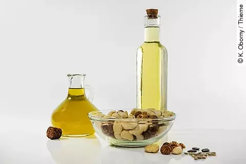 Beispiele für gesunde Fette: Pflanzenöle in Flaschen, eine Schale mit Nüssen