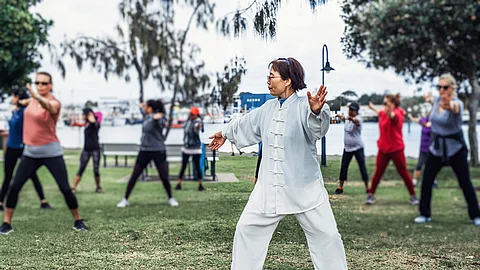 Chinesische Frau praktiziert Tai Chi mit einer Gruppe im Park