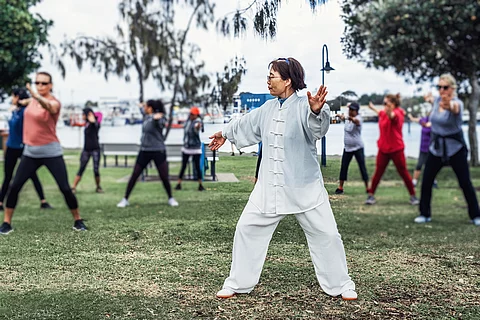 Chinesische Frau praktiziert Tai Chi mit einer Gruppe im Park