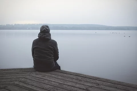 Mensch sitzt aus Steg und schaut auf See