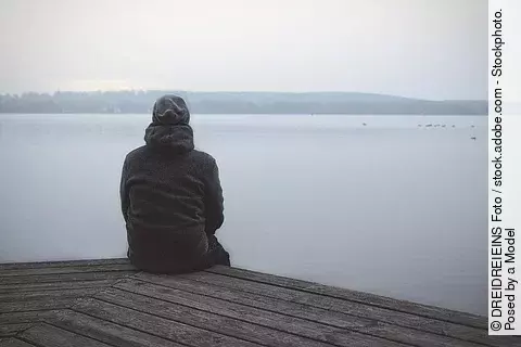 Mensch sitzt aus Steg und schaut auf See