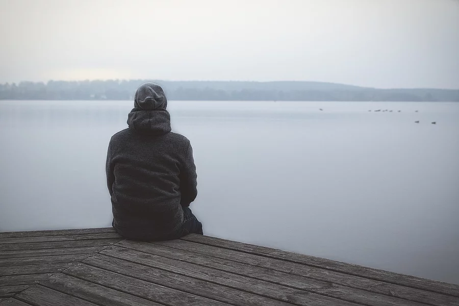 Einsamer Mann sitzt auf Steg am See oder Fluss / Lonesome Huy At Mensch sitzt aus Steg und schaut auf See