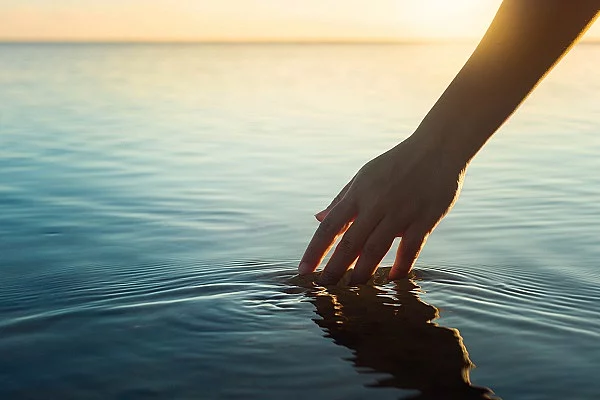 Eine weibliche Hand berührt die Wasseroberfläche von einem See.