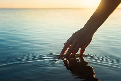 Eine weibliche Hand berührt die Wasseroberfläche von einem See.