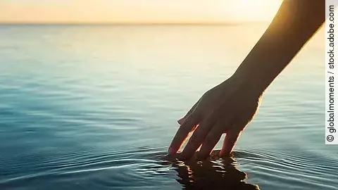 Eine weibliche Hand berührt die Wasseroberfläche von einem See.