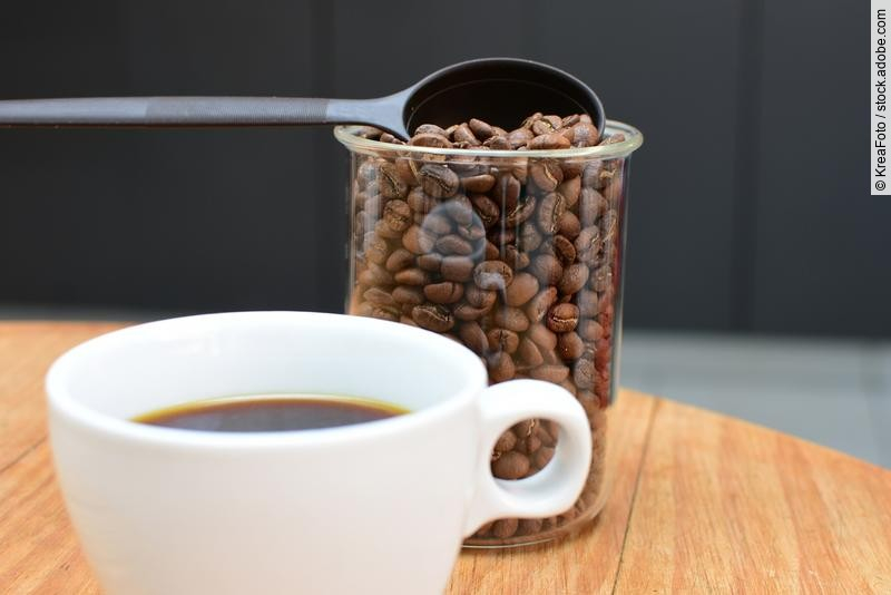 Tasse Kaffe und Plastikgefäß mit Kaffeebohnen auf einem Holztisch