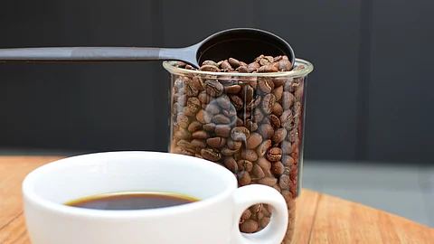 Tasse Kaffe und Plastikgefäß mit Kaffeebohnen auf einem Holztisch