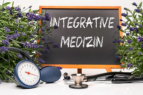 Tafel mit Aufschrift Integrative Medizin, daneben Lavendelbusch und Stethoskop