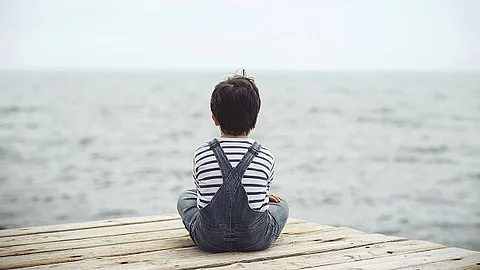 Kind sitzt im Schneidersitz und blickt auf das Meer.