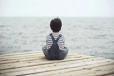 Kind sitzt im Schneidersitz und blickt auf das Meer.