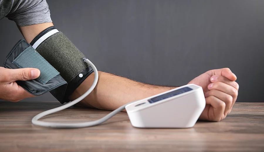 Caucasian man measuring his blood pressure at home. Mann misst Blutdruck, Arm liegt auf Holztisch