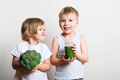 2 Kinder mit Lebensmitteln, eins lacht, das andere verzieht das Gesicht