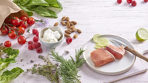 Mandeln, Lachs, Limette, Tomaten, Himbeeren, Spinat, Rosmarin, Thymian auf weißem Holzuntergrund