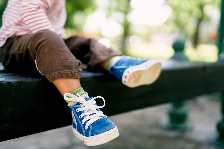Little baby feet in blue sneakers. Close-up Kleinkind sitzt auf einem Baumstamm