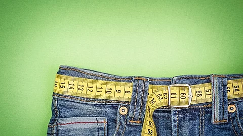 Ausschnitt einer Jeans mit Maßband als Gürtel auf grünem Hintergrund.