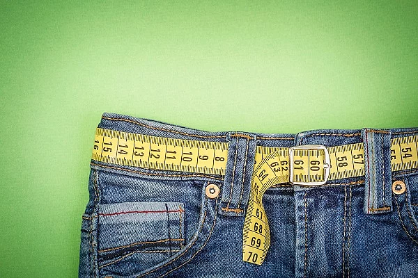 Ausschnitt einer Jeans mit Maßband als Gürtel auf grünem Hintergrund.